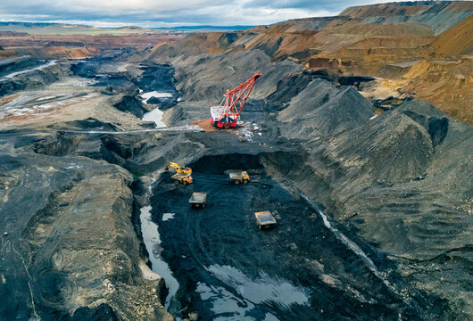 Aerial panoramic view captures industrial scale coal mining operation featuring large dragline excavator and multiple haul trucks