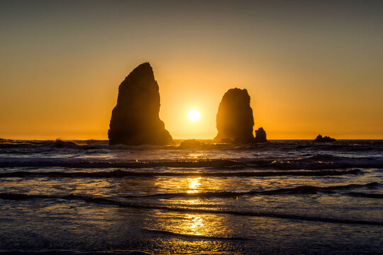 Golden sunset over Cannon Beach on the Oregon coast with iconic sea stacks silhouetted at popular American tourism destination.
