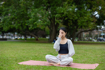 Fototapeta premium Young woman practicing alternate nostril breathing yoga in park