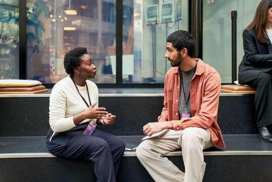 Female business expert discussing ideas with male executive while sitting on steps at networking event in convention cen