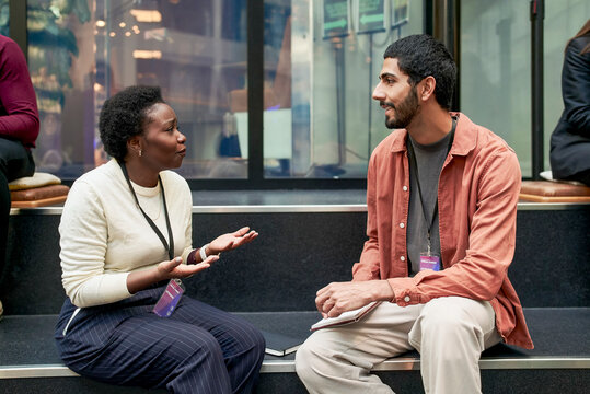 Female business expert discussing ideas with male colleague while sitting on steps at networking event in convention cen