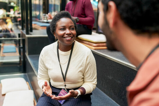 Smiling female business expert discussing ideas with male colleague while sitting on steps in convention center