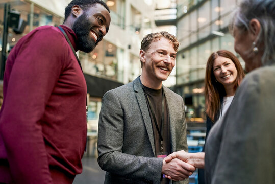 Smiling mature businessman greeting senior female expert with handshake at meet and greet event in congress center