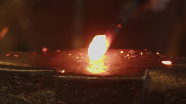 Close-up of a glowing metal tip being hammered repeatedly on an anvil, sparks flying with each strike, showcasing blacksmithing, craftsmanship, and dramatic forge action.