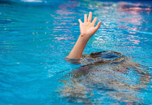Child hand of a sinking person reaching out of the blue water for rescue, emergency situation