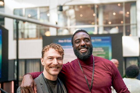 Portrait of smiling mature businessman standing with arm around colleague in convention hall