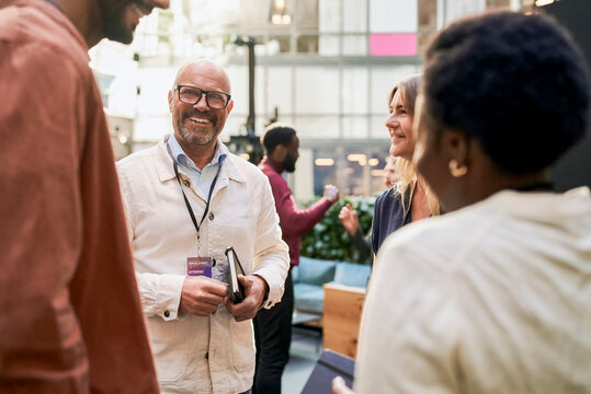 Smiling senior male entrepreneur discussing with business people at networking event in convention center