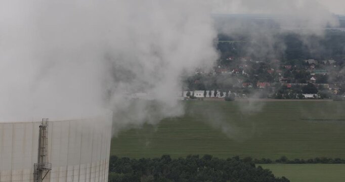 Telephoto shot of the upper section of a cooling tower at Schwarze Pumpe emitting heavy vapor, with a rural landscape in the background, symbolizing the German Kohleausstieg.