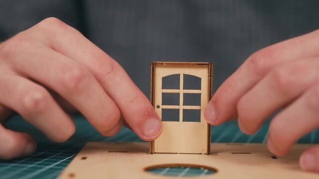 Installing top transom piece above wooden front door in miniature house model. DIY architecture crafting featuring plywood assembly and creative home construction hobby. Residential design concept