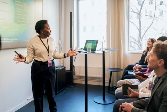Female presenter sharing ideas while giving presentation to associates at business summit in convention center