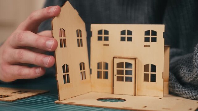 Installing wall panel during wooden house model construction. Hands assembling miniature home structure, DIY housing project, architectural crafting process, new property concept. Creative building