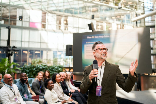 Happy mature male presenter speaking into microphone during summit at convention center