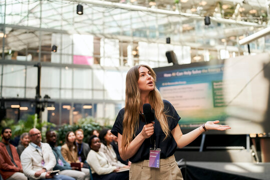 Long haired professional female speaker addressing seated audience about connectioneering during business session in con
