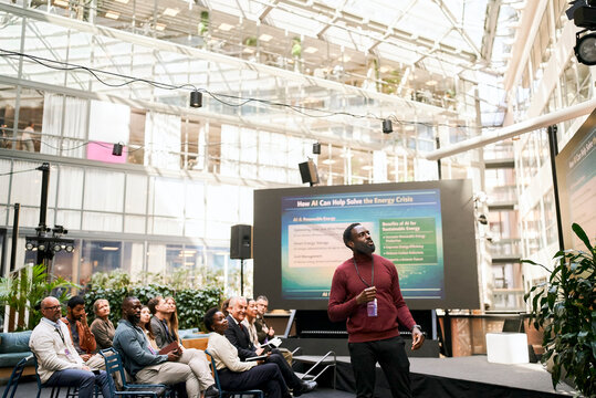 Male presenter giving presentation on how AI can help solve energy crisis to professional audience at summit in conventi
