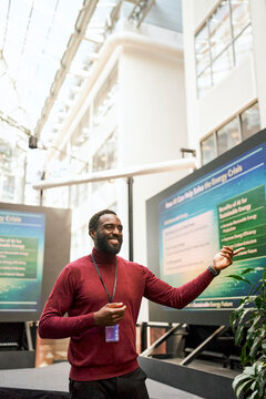 Smiling male presenter explaining slide show through projection show at summit in conference hall