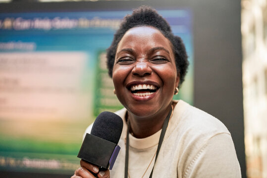Portrait of happy short haired female presenter holding microphone at seminar in convention center