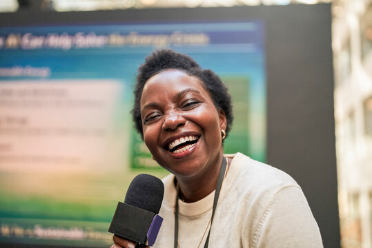 Portrait of happy short haired female presenter holding microphone at seminar in convention hall