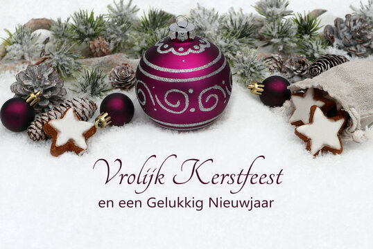 Paarse kerstbal omgeven door dennenappels, kaneelsterren en kleine paarse bolletjes op sneeuw met de Nederlandse kerstgroet Vrolijk Kerstfeest en een Gelukkig Nieuwjaar.