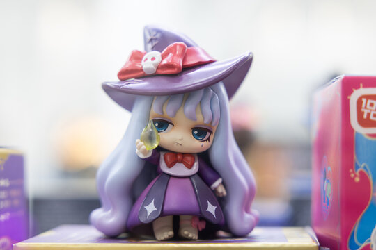 Designer art toy witch doll in purple dress and hat on blurred background
