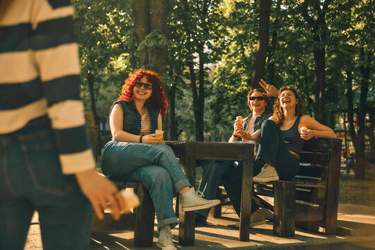 Friends relaxing at park table and greeting newcomer with vintage effect. Concept of casual meetup, social connection, summer lifestyle, outdoor rest, and welcoming mood.
