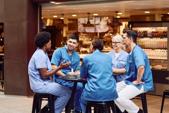 Team of medical experts talking with each other while sitting at table in hospital cafeteria