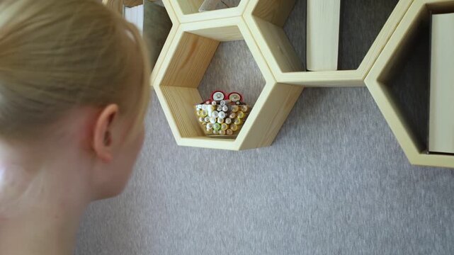 A young woman places a glass bowl filled with used batteries onto a wooden shelf for future disposal. This process demonstrates conscious household waste sorting and care for the environment.