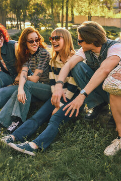 Young friends laughing on grass in sunny park with retro effect. Concept of carefree friendship, summer leisure, youth lifestyle, outdoor bonding, and nostalgic social mood.