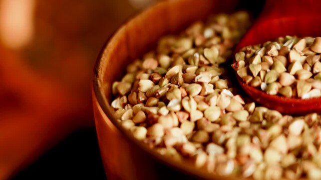 Scooping organic green buckwheat from wooden bowl with red spoon