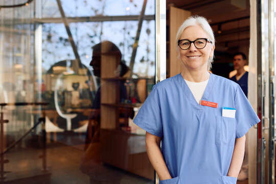 Portrait of confident senior female physician standing with hands in pockets