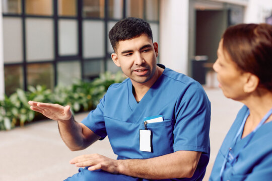 Young male healthcare expert gesturing while talking with female coworker in hospital lobby