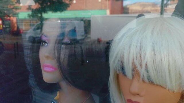 Stylized mannequin heads wearing fashion wigs in boutique window with reflective city traffic background. Beauty retail display presenting hairstyling trends luxury cosmetics mood and urban consumer