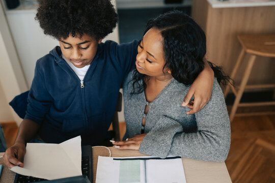 High angle view of son studying while sitting with arm around mother at home