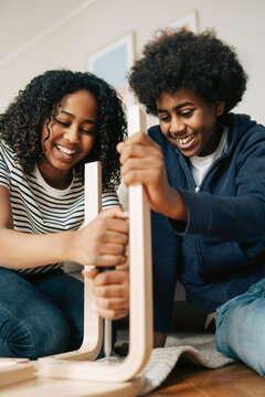 Happy boy helping sister tightening screw of wooden chair at home