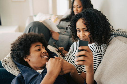 Boy sharing smart phone with sister sitting on sofa with family at home