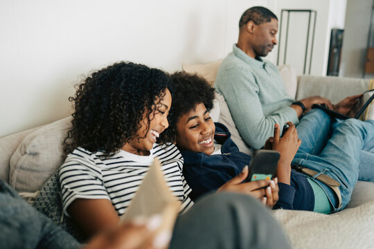 Happy children spending leisure time using phones while sitting on sofa at home