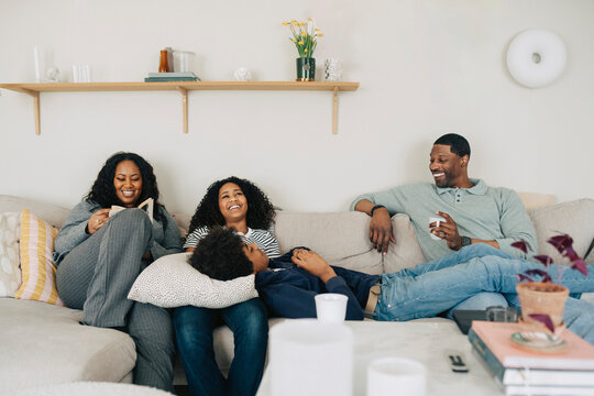Happy family members sitting together on comfortable sofa against wall at home