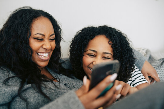 Happy mother and daughter spending leisure time using smart phone at home