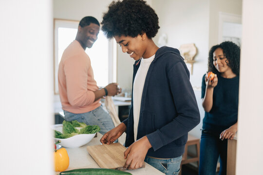 Smiling boy keeping cutting board on counter while preparing food in kitchen at home
