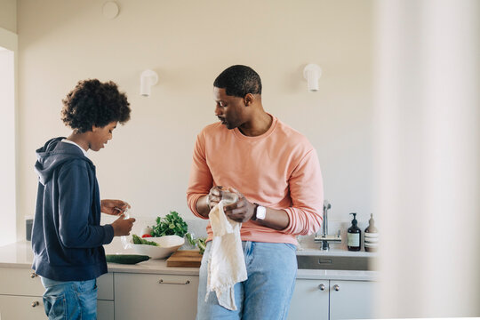 Son helping father while preparing food in kitchen at home