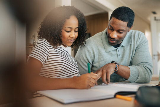 Mature man explaining lesson to daughter writing in book at home