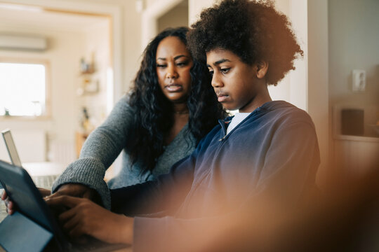 Woman assisting boy doing studies through tablet PC at home