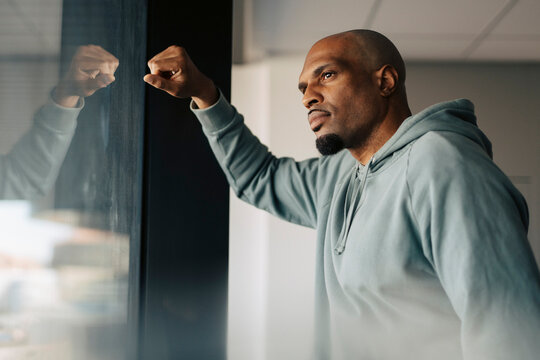 Thoughtful businessman with shaved head looking through glass window at office