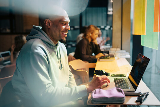 Smiling businessman scrolling laptop while sitting at desk and scrolling laptop in modern coworking hub