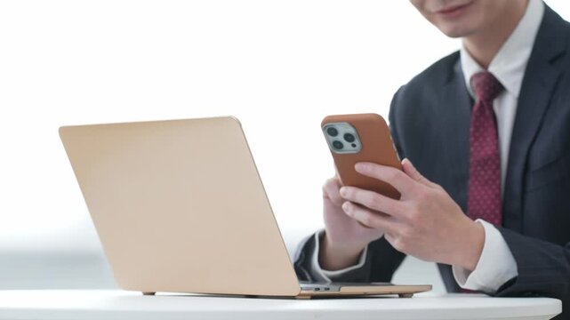 オフィスでノートパソコンとスマホを使う男性ビジネスパーソン