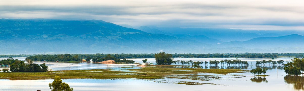 Aerial view of flooded plains with green islands and trees against a backdrop of blue mountains under a cloudy sky Sunamganj, Sylhet Division, Bangladesh.