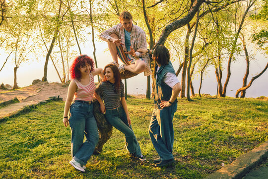 Friends talking by lakeside tree in warm vintage color grading. Concept of campus life, group therapy, community, friendship stories, mental wellness, and relaxed outdoor leisure.