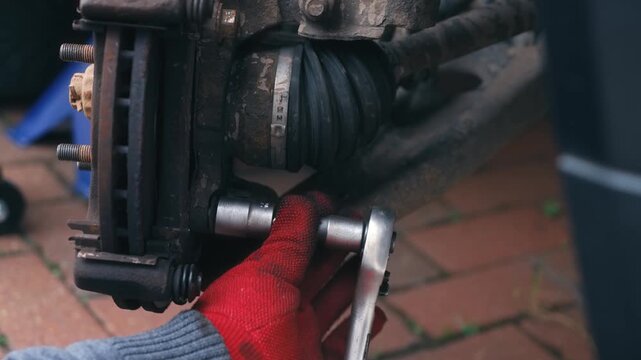 Undoing brake mounting fasteners with ratchet socket during car repair procedure. Dismantling braking hardware from disc assembly for vehicle maintenance outdoors. Automotive mechanical work focusing