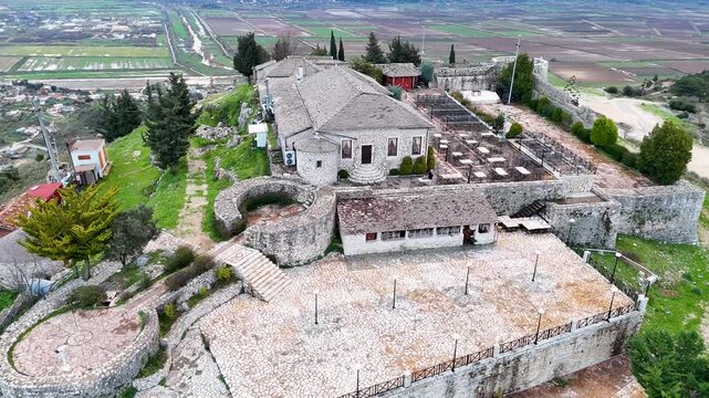 High angle aerial shot overlooking the expansive stone terraces, pathways, central stone restaurant, and surrounding battlements of Lekuresi Castle in Sarande, Albania