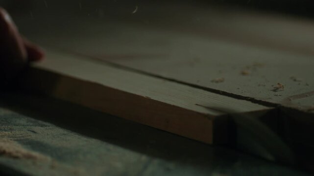 inematic close-up of a wooden board being planed and smoothed on a jointer machine in a carpentry workshop. Woodworking concept highlighting fine shavings and timber texture.
