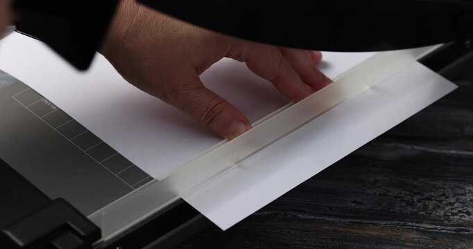 The hand cuts the edge of the paper with a mechanical cutter guillotine 